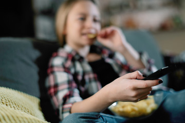 Young girl watching TV. Cute little girl eating snacks and enjoying on sofa 