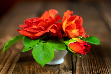 A small vase of red roses on a wooden table.