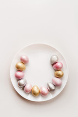 Colored painted pearl chicken and quail eggs of pink, silver golden color on a purple plate pastel background. Minimalistic creative idea easter festive vertical wallpaper flat lay. Copyspace for text