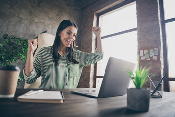 Photo of attractive latin business lady raise fists look notebook table chatting colleagues read startup success information letter wear striped shirt sit chair modern office indoors