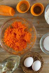 Grated carrot, eggs, oil, sugar, flour, spices as ingredients for carrot pie on the wooden background