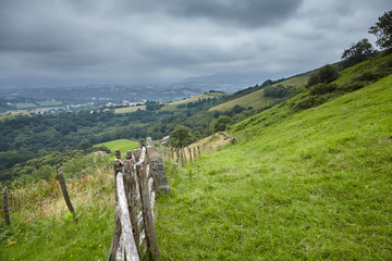 Foothills of the Pyrenees. Rural landscape with a old wooden farm fence. Hillsides covered with green grass at cloudy summer day. Hilly countryside, Sare, France, Europe