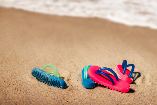 Two pairs of beach sandals or thongs on a sandy beach and seashore on background with free copy space.