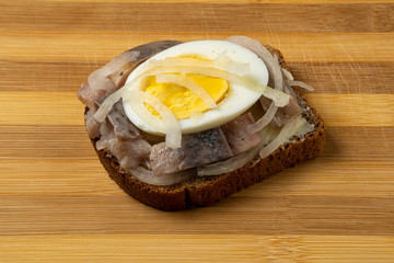 Sandwich with herring, onions and chicken egg on a wooden tray. National Russian cuisine