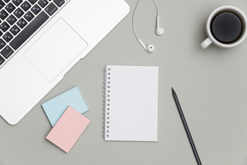 Blank notepad over laptop and headphones on gray office table