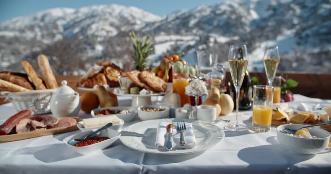 Close up shot of a luxurious breakfast with various fruits, snacks and champagne served on terrace with beautiful view on winter mountains - luxury lifestyle concept 4k footage