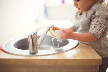 Toddler child washes dishes in sink