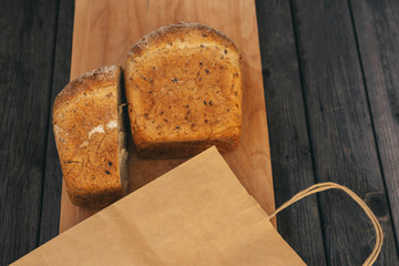 Fresh homemade bread with sunflower seeds, isolated on a wooden background with an eco-friendly Kraft paper bag. Side view, close-up.