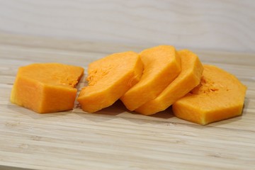 The interior of a soft orange-coloured pumpkin is cut with pieces on a board before making porridge or soup