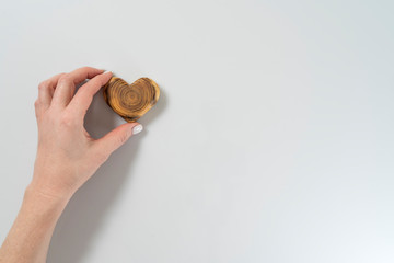 young woman's hand holds a wooden heart, a gift for Valentine's day, white background, copy space on the right, horizontal frame