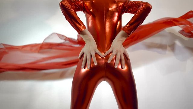 Tracking shot from between the hips  of slender girl in a tight shiny red zentai suit with red flying lace. Isolated on  white studio background. 4k 100 fps slow motion