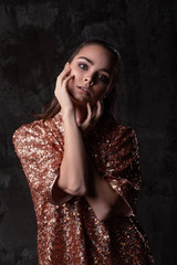 Fashion portrait of a young woman in a studio lights. Girl model touches her face with fingers. Wet hairstyle and smokey eyes.