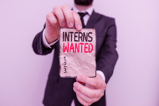 Text sign showing Interns Wanted. Business photo showcasing temporary position with an emphasis on the job training Male human wear formal work suit office look hold notepaper sheet use hand - Powered by Adobe