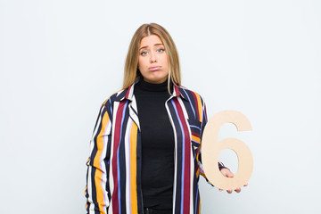 young pretty blonde woman sad, depressed, unhappy, holding a number 6.