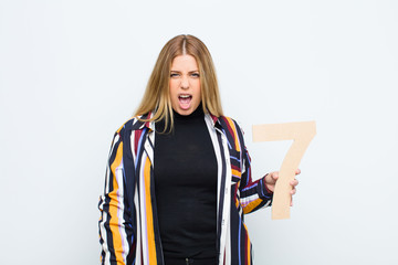 young pretty blonde woman angry, anger, disagreement, holding a number 7.
