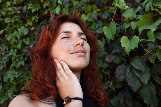 Portrait of a red-haired dreaming girl near a wall from a plant.