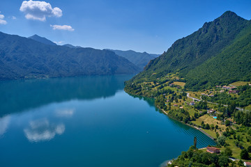 Naklejka na ściany i meble Panoramic view of the mountains and Lake Idro. Reflection in the water of the mountains, trees, blue sky. Aerial view, drone photo