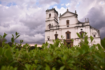 Fototapeta na wymiar Picture of a white church in goa with a green foreground and cloudy sky