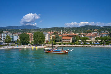 Fototapeta na wymiar Aerial photography. Beautiful coastline. In the city of Bardolino, Lake Garda is the north of Italy. View by Drone. Large sailboat parked in port.