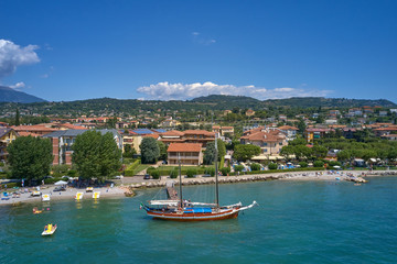 Fototapeta na wymiar Aerial photography. Beautiful coastline. In the city of Bardolino, Lake Garda is the north of Italy. View by Drone. Large sailboat parked in port.
