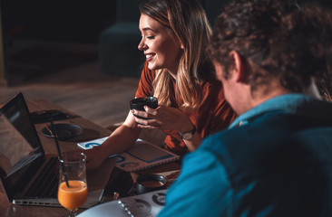 Group of students sitting in cafe using laptop drinking coffee and talking about next project.
