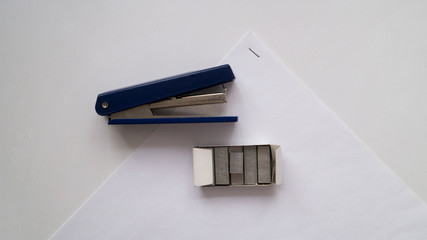 Blue small paper stapler with brackets in the package on the background of a white sheet of paper.