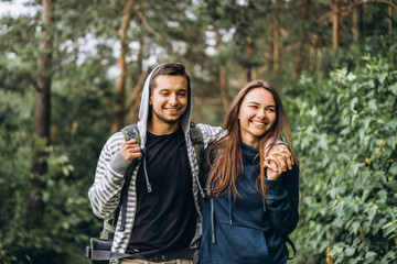 Young couple with backpacks on their backs smiling and walking in the forest, enjoy the walk