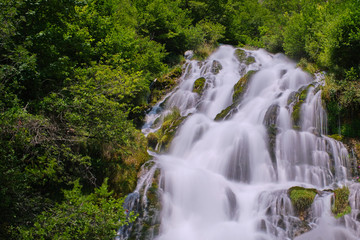 Fototapeta na wymiar Wild, large waterfall, long exposure along green thickets. White water drop down