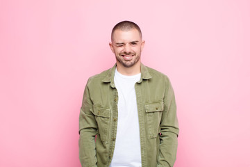 young handsome man looking happy and friendly, smiling and winking an eye at you with a positive...