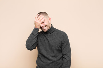 young handsome man laughing and slapping forehead like saying d‚Äôoh! I forgot or that was a...