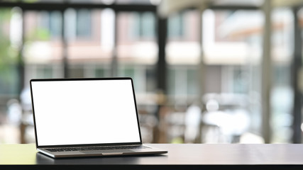 Photo of computer laptop with white blank screen putting on the modern working table with blurred comfortable office as background. Void screen for advertise concept.