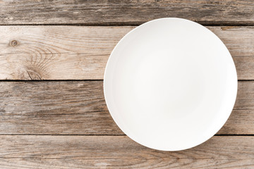 Overhead shot of empty white plate on rustic wooden table. Close up