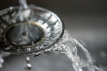 Close up of water running over the edge of a metal rinsing strainer