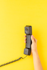 Woman’s hand holding retro phone on yellow background with copyspace. Hotline concept