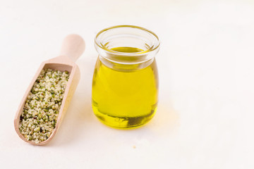 hemp oil in a glass bottle next to hemp peeled seeds on a white background with copy space