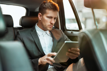 young businessman reading world daily news while sitting in his car on his way to office, multitasking concept