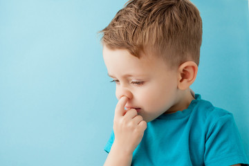 Little caucasian boy picking his nose on blue background - obrazy, fototapety, plakaty