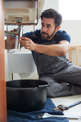 Male Plumber Working To Fix Leaking Sink In Home Bathroom