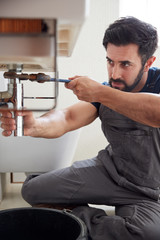 Male Plumber Using Wrench To Fix Leaking Sink In Home Bathroom