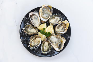 Fresh oysters seafood on a black plate background - Open oyster shell with herb spices lemon rosemary served table and ice healthy sea food raw oyster dinner in the restaurant gourmet food