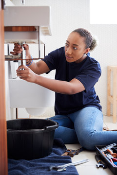 Female Plumber Working To Fix Leaking Sink In Home Bathroom