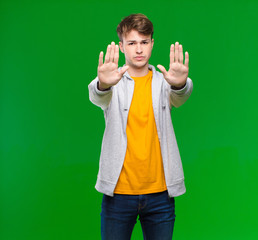 young blonde man looking serious, unhappy, angry and displeased forbidding entry or saying stop...