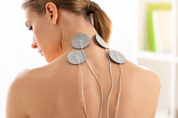 Back view of beautiful woman with electrodes on neck during electrotherapy in clinic - Powered by Adobe