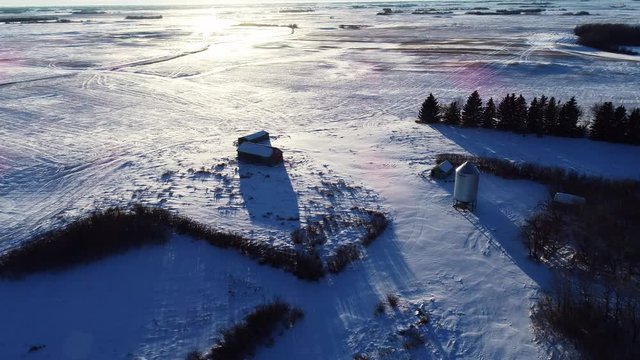 Westbound drone flyover of some granaries in a snow-covered field.