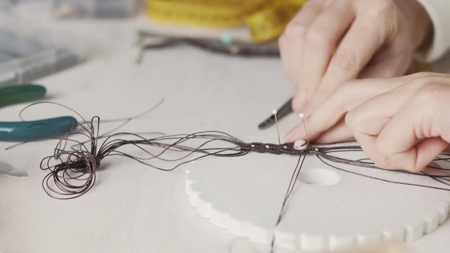Lifestyle concept, work from home to reinvent your life: close-up of woman hands making macrame knotted jewelry with stone beads and tools on light wooden table