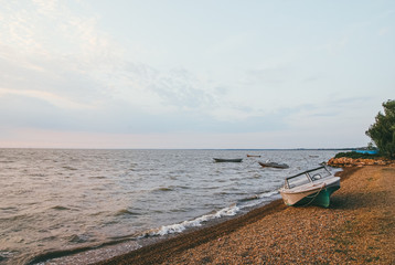 Group of fishing motor boats in the sea against the background of the evening sunset sky. They are ready to go fishing. One boat on a shingle bank in the foreground