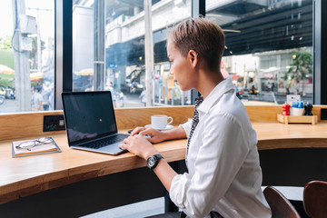 Beautiful young business woman using computer while sitting in cafe. She plans her business...