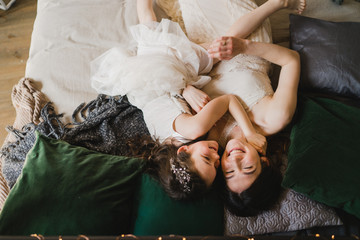 Mother and daughter hugging and cuddling in bed. Pretty little girl and beautiful woman lie together. Girls in lace dresses playing in decorated room. Family weekend, beauty day, having fun, love.