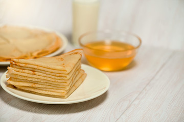 Fototapeta na wymiar Maslenitsa is a holiday at the end of February . pancakes with honey and milk on a light wooden background. honey trickles down a stack of pancakes. close up. blini. space for text