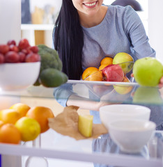 Smiling woman taking a fresh fruit out of the fridge, healthy food concept